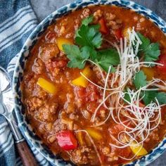 a blue and white bowl filled with chili, meat and noodles next to a spoon