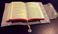 an open book sitting on top of a wooden table next to a small beaded necklace