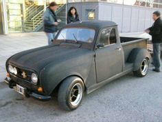 an old pick up truck parked in front of a building with people looking at it