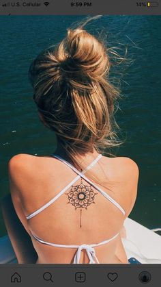 a woman with a tattoo on her back sitting in a boat looking out at the water