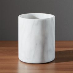 a white marble vase sitting on top of a wooden table next to a gray wall