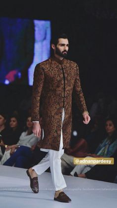 a man walking down the runway wearing a brown and black outfit with an intricate pattern on it