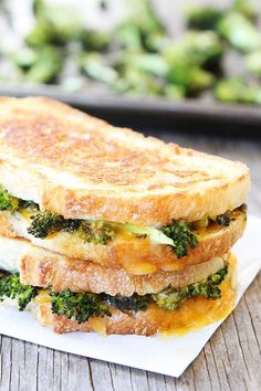 a grilled cheese and broccoli sandwich on a white plate with a tray of broccoli in the background