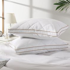 two pillows stacked on top of each other in front of a bed with white sheets