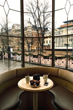 two coffee cups sitting on top of a round table in front of a large window