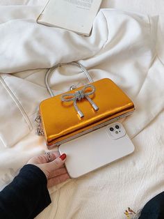 a woman is holding an orange purse with a bow on the front, and a white phone in her hand