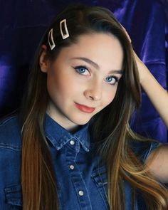 a young woman with long hair and blue eyes is wearing two metal clips on her head