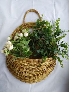 a wicker basket filled with flowers and greenery on a white tablecloth background