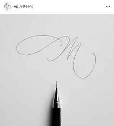 a pen is writing on paper with the letter m in cursive writing,