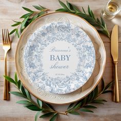 a baby shower plate with greenery around it on top of a wooden table next to utensils