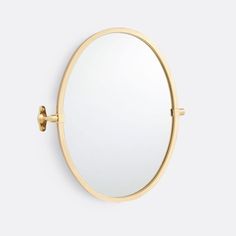 a round mirror mounted to the side of a wall with a gold frame and metal fittings