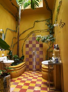 a bathroom with yellow walls and checkered tile flooring, potted plants in the corner