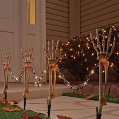 three skeleton hand torches in front of a house with christmas lights on the trees behind them