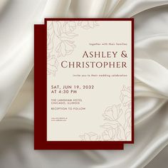 an elegant wedding card with white and red flowers on the front, along with a burgundy border