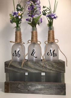 three vases with flowers tied to each other on a shelf in front of a wall