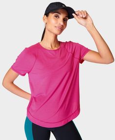 a woman in a pink shirt and black cap posing for the camera with her hands on her head