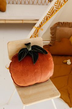 an orange pumpkin pillow sitting on top of a wooden chair next to a white wall