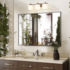 a bathroom vanity with a large mirror above it and plants on the wall behind it