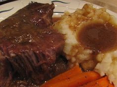 a white plate topped with meat, potatoes and carrots next to gravy