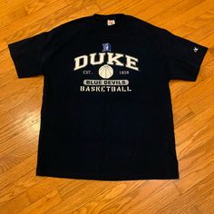 a black duke basketball t - shirt sitting on top of a wooden floor