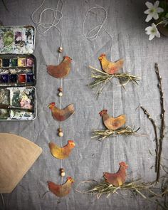 some little chickens are hanging on the string next to some flowers and paintbrushes