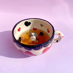 a tea cup with a dog in it on a purple surface, filled with hearts