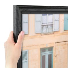 a hand holding up a framed photograph of an old building with shutters and windows