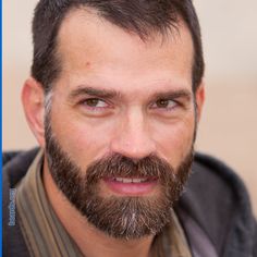 a man with a beard and striped shirt looks at the camera while he is smiling