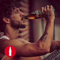 a man drinking beer while holding a guitar in his right hand and playing the guitar