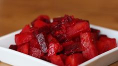 a white square bowl filled with cut up fruit on top of a wooden table next to a knife