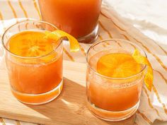 two glasses filled with orange juice sitting on top of a wooden cutting board next to an orange slice