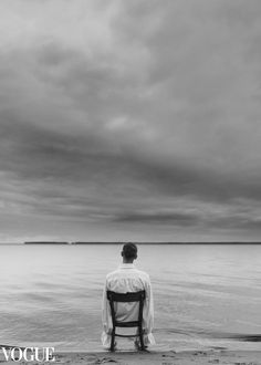 a man sitting in a chair looking out at the ocean on a cloudy day with an overcast sky