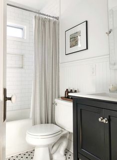 a white toilet sitting next to a sink in a bathroom under a window with curtains