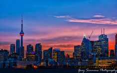 the city skyline is lit up at night with bright lights and clouds in the sky