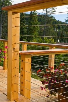 a wooden deck with flowers growing on the railing and in the background is a wooded area