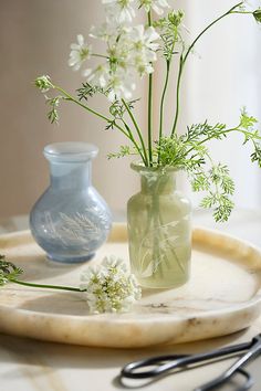 two vases with flowers in them sitting on a tray