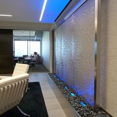 an office lobby with a wall fountain and white chairs in front of the glass windows