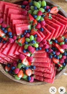 watermelon, grapes, and strawberries are arranged on a wooden platter