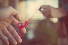 a person is holding a red string with one hand and the other hand has a pair of scissors in it