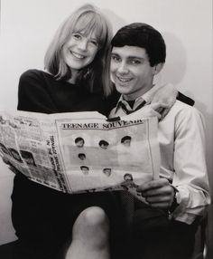 a man and woman sitting next to each other while holding a newspaper with pictures on it