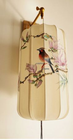 a lamp with a bird painted on it hanging from a wall next to a flowery branch