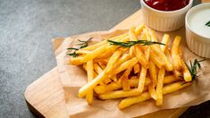 french fries on a cutting board with dipping sauces