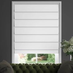 a living room with a couch and window covered in white roman blind shades on the windowsill