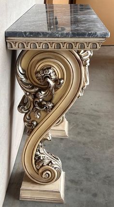 an ornate table with marble top in the shape of a letter s on concrete flooring