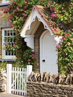 a house with pink flowers growing over it's roof and door, next to a white picket fence