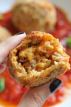 a hand holding up a piece of food in front of some vegetables and meatballs