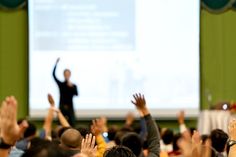 many people are raising their hands in front of a screen with a man on it