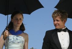 a man and woman in formal wear standing under black umbrellas, looking at each other