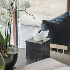 a vase with flowers and tissue paper on a table in front of a window, next to a black chair