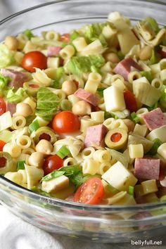 a salad in a glass bowl with tomatoes, lettuce, ham and olives